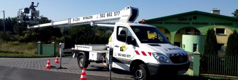 Pojawiło się wyzwanie na wysokości. Decydujesz się na użycie zwyżki – to ona najlepiej sprawdzi się w tym zadaniu. Jaki jest koszt wynajmu podnośnika koszowego i od czego zależy? Odpowiadamy. Od czego zależy cena wynajmu wysięgnika koszowego? Koszt wynajmu zwyżki jest uzależniony od wielu czynników. Poniżej wyjaśnimy, w jaki sposób parametry maszyny i doświadczenie firmy przekładają się na wysokość ponoszonej opłaty. 1. Wysokość podnośnika koszowego Tak jak można się domyślać, cena wzrasta wraz z wysokością. Jest to związane między innymi z tym, że im wyższy wysięgnik, tym większy samochód, na którym się znajduje i bardziej konkretna maszyna. Oddziaływanie sił musi się zgadzać! Do tego dochodzi również eksploatacja dużej zwyżki – większy samochód pali więcej, i to także wpływa na koszt wynajmu podnośnika koszowego. 2. Udźwig kosza wysięgnika koszowego Wraz z wyższymi parametrami, które są istotne w pracach na wysokości, wzrasta cena wynajmu zwyżki. Jednym z nich jest udźwig kosza. Zwyżka transportuje do góry różne ciężary. Oprócz masy ludzi w jej wnętrzu trzeba tu także wliczać masę narzędzi. Podnośnik koszowy często uczestniczy w realizacjach, gdzie np. przykręca, czy spawa się coś na wysokościach. Wysięgnik dysponujący większym udźwigiem kosza, oznacza wyższą cenę za jego wynajem. Jednak dzięki temu parametrowi pracę wykonuje się szybciej. Na platformie roboczej może pracować więcej osób - skracając czas realizacji. 3. Rodzaj podwozia zwyżki budowlanej Maszyny mają swoje ograniczenia co do miejsc, w które mogą wjechać. Czasem na drodze stają zlecenia, gdzie podwozie terenowe ratuje całą akcję. Wiemy to z doświadczenia, bo nasza firma właśnie w takich sytuacjach pomaga Klientom podnośnikiem koszowym H – 45 lub podnośnikiem koszowym H-70. Zwyżki te dają radę wszędzie tam, gdzie inne się poddają. A wszystko to za sprawą podwozia 4 x 4. Wyższy koszt wynajmu takich maszyn jest zatem uzasadniony. 4. Doświadczenie operatora Doświadczenie osoby kierującej maszyną daje duży komfort pracy. Zwyżka może być sterowana przez pracowników z kosza podnośnika, ale również z pomocą operatora z dołu. Można spodziewać się, że podnośnik koszowy (cena wynajmu) będzie droższy w przypadku firm posiadających pracowników z wieloletnim doświadczeniem. Poza sterowaniem kosza, ich kunszt może ułatwić wiele zleceń u Klientów. Wprawa i praktyka pozwala im zaproponować nowe rozwiązania, ale także uniknąć groźnych sytuacji. 5. Jakość usług Jak to bywa w świecie usług, na rynku są firmy, które świadczą je podnośnikami koszowymi długo i takie, które ledwie co zaczęły. Doświadczenie w branży przekłada się na oferowaną jakość oraz cenę. Również stan maszyn i ich wiek mają wpływ zarówno na koszt usługi, jak i na jakość. Młodsze zwyżki i wysięgniki będą charakteryzować się mniejszą liczbą usterek czy awarii. Jest to również aspekt determinujący cenę wynajmu. Pomimo tego, że obowiązkiem operatorów jest noszenie kasków, kamizelek odblaskowych, odpowiedniego obuwia, to są pracownicy, którzy wciąż te zasady bagatelizują. Można spodziewać się, że wypożyczalnie zwyżek wyceniających wyżej swoje usługi, będą ich nakłaniać i mobilizować do przestrzegania tych podstawowych wymogów bezpieczeństwa. Usługa podnośnikiem koszowym – jakiej ceny możesz się spodziewać? Na rynku krakowskim ceny najczęściej zaczynają się od 100 złotych za godzinę. Za taką opłatą otrzymamy podnośnik koszowy o wysokości 22 metrów. Później wraz ze wzrostem wysokości i innych parametrów, wzrasta też odpowiednio cena zwyżki. Podnośnik koszowy – cena w Krakowie a w mniejszych miastach. W czwartek późnym popołudniem nasz dyspozytor odbiera telefon od Klienta. - Witam serdecznie Panie Karolu. Potrzebuję wesprzeć pracę swojej Ekipy przy montażu liter przestrzennych w przyszły poniedziałek i wynająć 22 – metrowy podnośnik koszowy. Czy możemy liczyć na maszynę? Karol sprawdza kalendarz. Klient wstrzelił się idealnie, gdyż w poniedziałek akurat mamy 5-godzinne okienko dla tej zwyżki. Wpisuje zatem zamówienie na godzinę 11:00. Na umówionym zleceniu nasz operator Paweł stawia się 10 minut wcześniej, żeby rozeznać teren i rozłożyć wysięgnik koszowy. Po chwili jest już gotowy do działania. Ekipa montażowa składa się z 3 osób. Dwoje z nich będzie pracować z kosza podnośnika, a ostatni z dachu budynku. Dzięki temu będą mogli komfortowo osadzić litery. To do dzieła. Pierwszy pracownik wchodzi na górę budynku poprzez wewnętrzny właz, natomiast dwóch pozostałych już jest na obudowanej platformie zwyżki wraz z koniecznymi narzędziami. Operator steruje koszem bezpośrednio do miejsca pracy. Ekipa zabiera się za instalację reklamy. Zaczynają od naklejenia linii poziomującej, tak aby mieli pewność, że napis jest równo mocowany. Przechodzą do montażu pierwszej litery – jest nią „C”. Mężczyzna znajdujący się na dachu, podaje literę pracownikom w koszu zwyżki budowlanej. Ci od razu przechodzą do wkręcenia pierwszej śruby. Następnie proszą operatora Pawła: - Przesuń nas na odległość ok. 5-6 metrów od ściany w linii prostej, tak abyśmy mogli zobaczyć, czy na pewno jest równo. Paweł wedle ich instrukcji steruje obudowaną platformą. Dostaje sygnał, że wszystko jest w porządku. Mogą kontynuować. Przykręcają śruby i przechodzą do kolejnych liter. Procedura dalszego montażu przebiega podobnie, jak przy pierwszej literze – szybko i sprawnie. Po 3,5 godziny nowa reklama już zdobi budynek. Teraz będzie ona widoczna już z oddali. Po pracy jeden z pracowników zwraca się do Pawła: - Dzięki za działanie. Wszystko przebiegło wzorowo. Muszę się z Tobą jeszcze czymś podzielić. Na codzień pracujemy w mniejszej miejscowości 80 km od Warszawy. To zlecenie w Krakowie robiliśmy dla znajomego szefa. I wiesz co? Jestem pod wrażeniem, że macie tu niższe ceny niż u nas za wynajem zwyżki. A mówią, że duże miasto to wyższe ceny. Wciąż można się jeszcze zdziwić na tym świecie. Do zobaczenia następnym razem. Wyzwanie na wysokości? Jesteśmy do dyspozycji! A gdybyś potrzebował podnośnika koszowego, to śmiało kontaktuj się z nami pod numerem +48 502 602 577. Chętnie pomożemy w doborze maszyny odpowiedniej dla Twojego zlecenia!