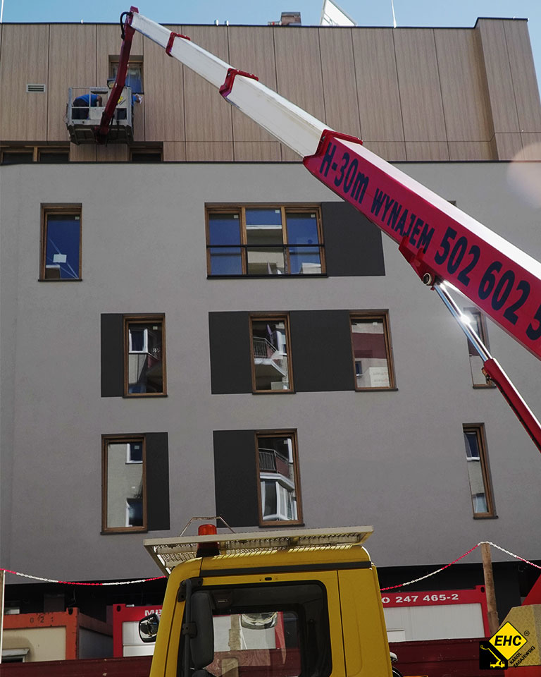 Czerwony podnośnik koszowy H-30 pomaga w czyszczeniu elewacji z kleju